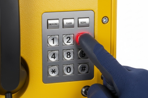 Gloved finger pressing emergency key on industrial phone keypad with backlit button