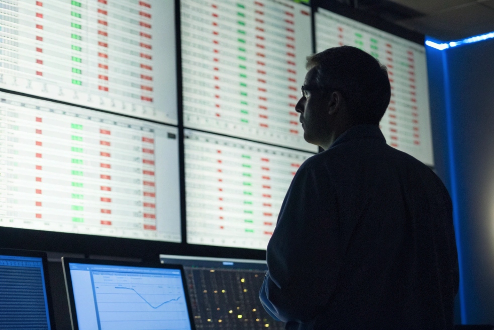 Operator standing in a dark network operations center, looking at a wall of large screens filled with VoIP call log tables of red and green status indicators.