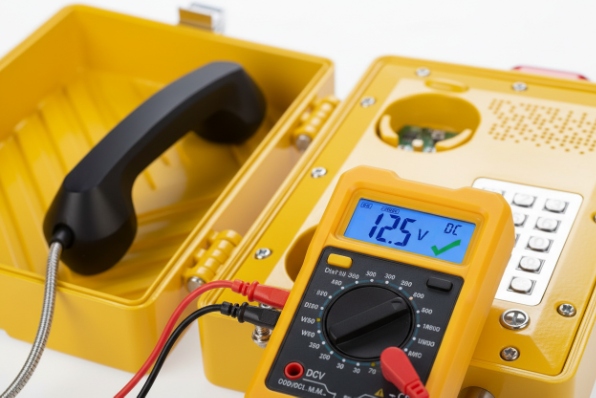 Multimeter measuring DC voltage on industrial phone wiring during bench diagnostics