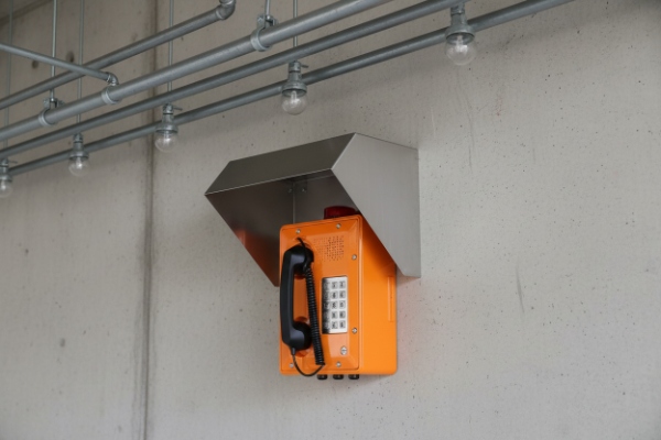 Wall-mounted industrial SIP emergency telephone with metal rain hood on concrete wall