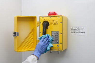 Technician wiping explosion-proof SIP phone keypad and handset during cleaning procedure in sterile room
