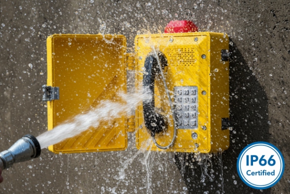 IP66 certified yellow emergency phone being pressure washed with water spray on concrete wall