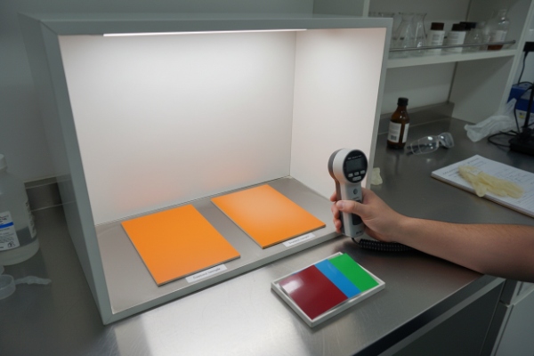 Color light booth measuring orange enclosure panels using handheld spectrophotometer
