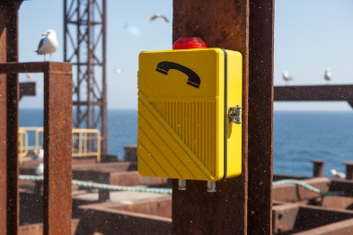 Closed yellow emergency telephone enclosure with beacon on offshore platform overlooking sea
