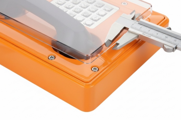 Caliper measuring protective cover thickness on orange industrial emergency phone keypad panel