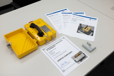 Open explosion-proof phone with compliance certificates and test documents on desk
