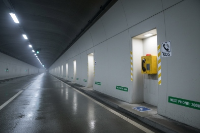 Long road tunnel with wall-mounted yellow SOS emergency telephone and distance signage