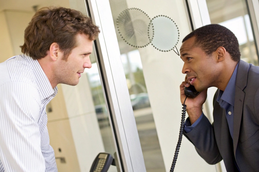 Building visitor talking on handset intercom with person inside lobby through glass door