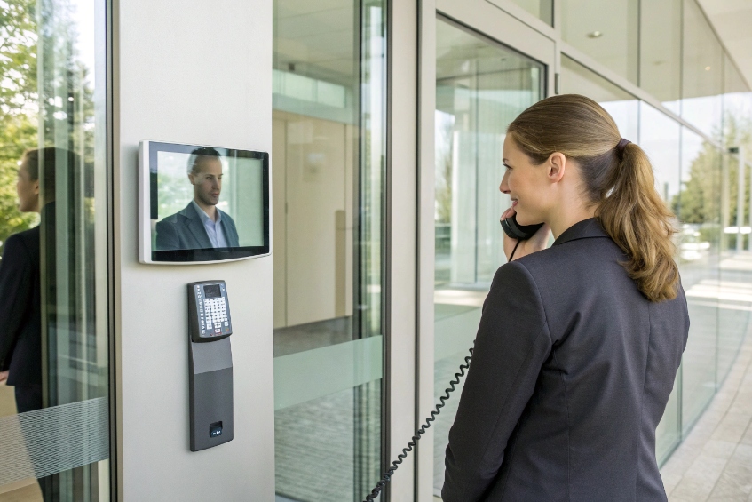 Receptionist speaking on handset to visitor shown on video door intercom screen