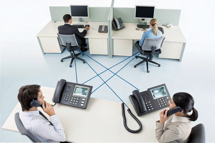Office employees talking on interconnected SIP desk phones in a shared workspace