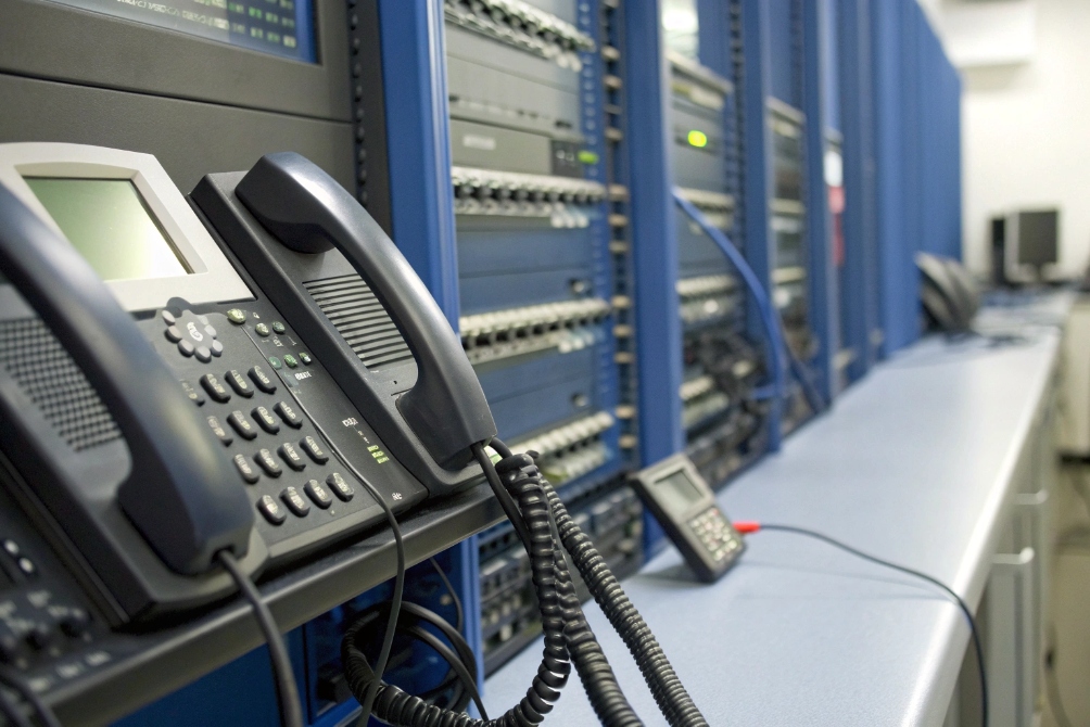 Row of SIP desk phones mounted beside telecom server racks in test lab