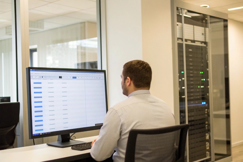 Network administrator monitoring SIP and video systems from workstation beside server rack